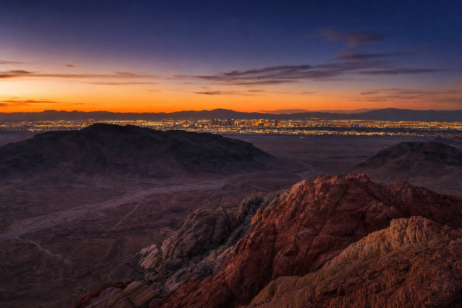 Las Vegas Strip lights at twilight seen from desert mountains.